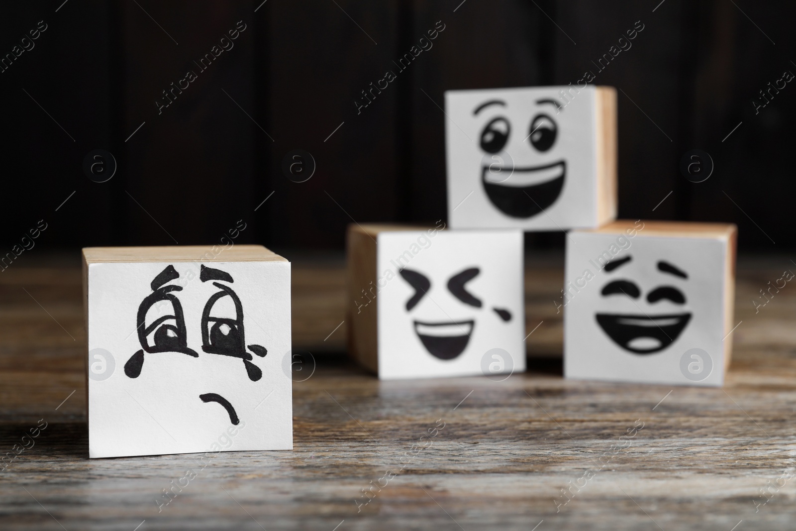 Photo of Cubes with sad and funny faces on wooden table. Bullying concept