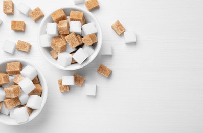 Photo of Different sugar cubes in bowls on white wooden table, flat lay. Space for text