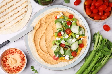 Tortilla with hummus and vegetables on white marble table, flat lay