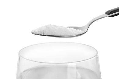 Spoon with baking soda over glass of water on white background