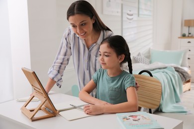 Mother helping her daughter doing homework with tablet at home