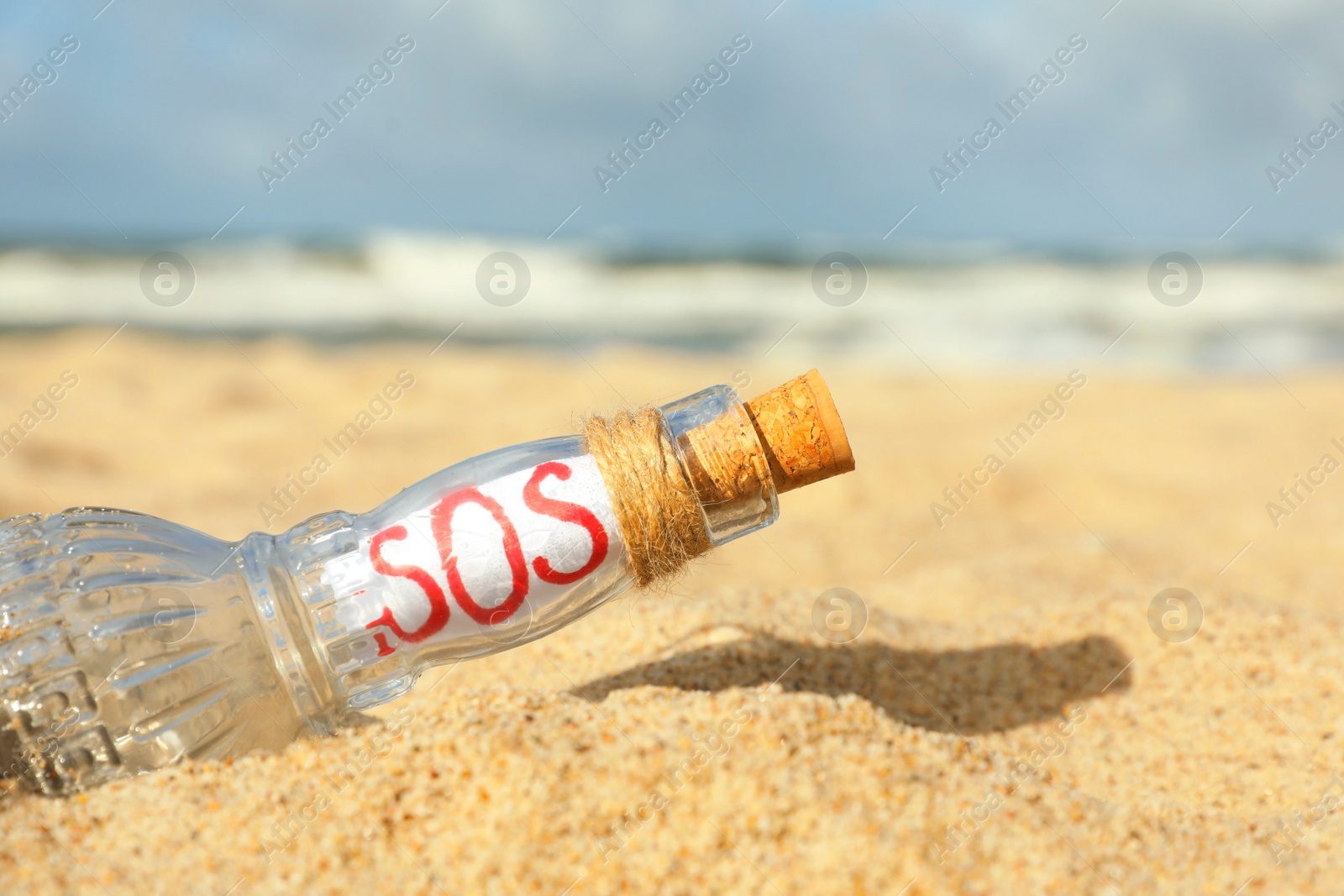 Photo of Glass bottle with SOS message on sand near sea, closeup