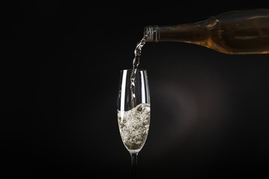 Photo of Pouring sparkling wine from bottle into glass on black background
