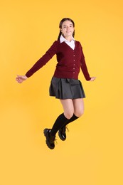 Photo of Teenage girl in school uniform jumping on yellow background
