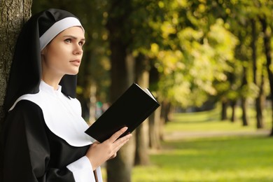 Young nun reading Bible in park on sunny day, space for text