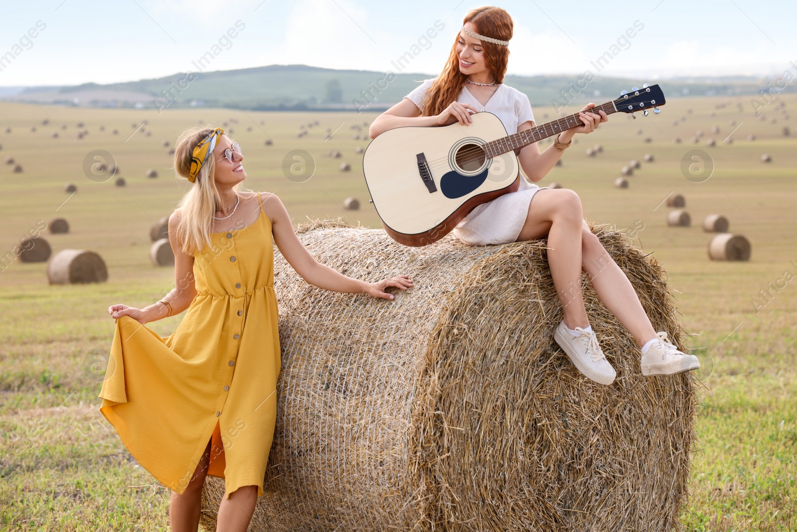 Photo of Beautiful hippie woman listening to her friend playing guitar in field