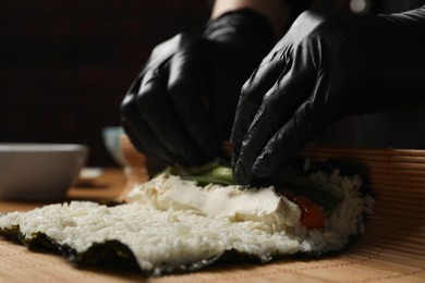 Photo of Chef in gloves making sushi roll at wooden table, closeup