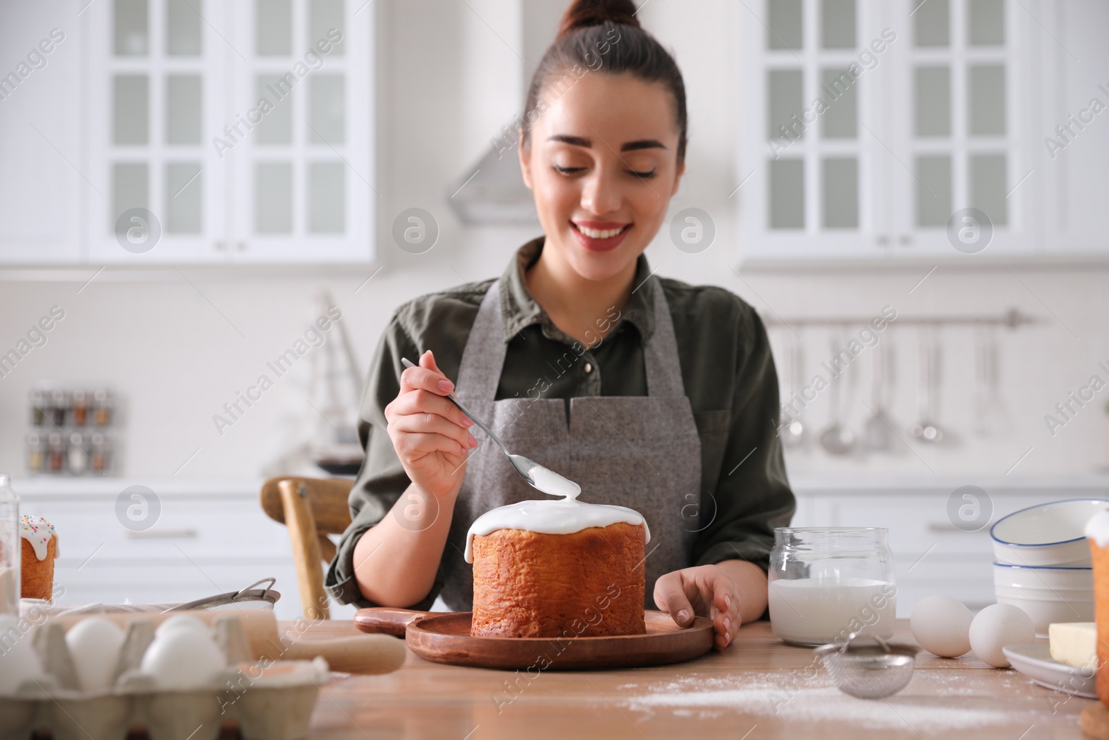 Photo of Young woman decorating traditional Easter cake with glaze in kitchen