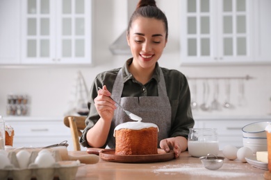 Photo of Young woman decorating traditional Easter cake with glaze in kitchen