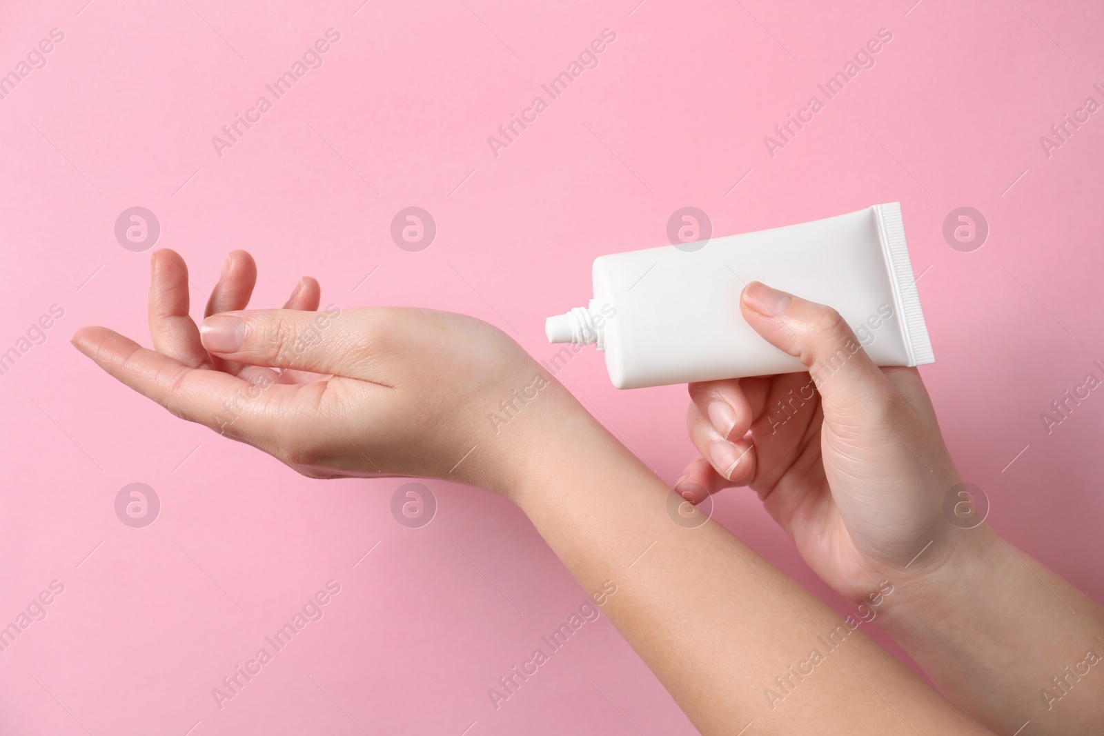 Photo of Woman applying cosmetic cream from tube onto her hand on pink background, closeup