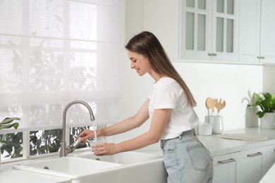 Woman filling glass with water from tap in kitchen