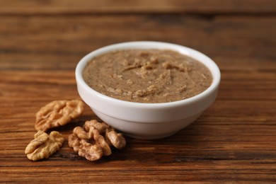 Photo of Delicious nut butter in bowl and walnuts on wooden table, closeup