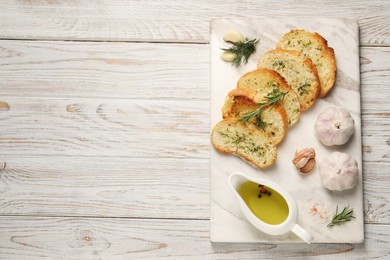 Photo of Tasty baguette with garlic, dill, rosemary and oil on white wooden table, top view. Space for text