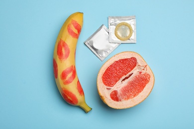 Photo of Condoms, cut grapefruit and banana with lipstick kiss marks on light blue background, flat lay. Safe sex