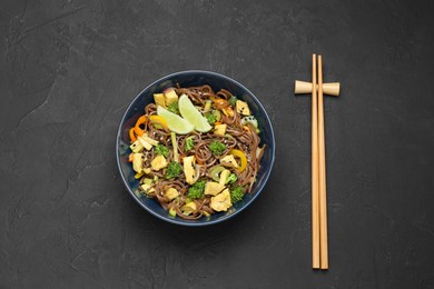 Photo of Stir-fry. Delicious cooked noodles with chicken and vegetables in bowl served on gray textured table, flat lay