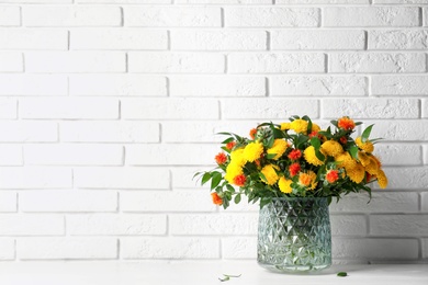 Photo of Bouquet with beautiful flowers in glass vase on white wooden table near brick wall. Space for text