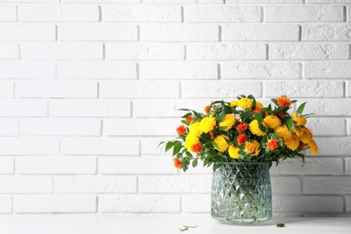 Bouquet with beautiful flowers in glass vase on white wooden table near brick wall. Space for text