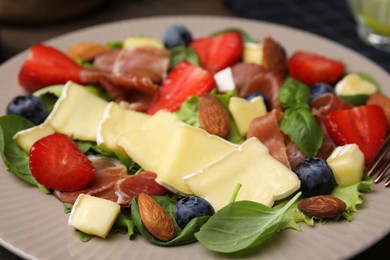 Tasty salad with brie cheese, prosciutto, almonds and berries on plate, closeup