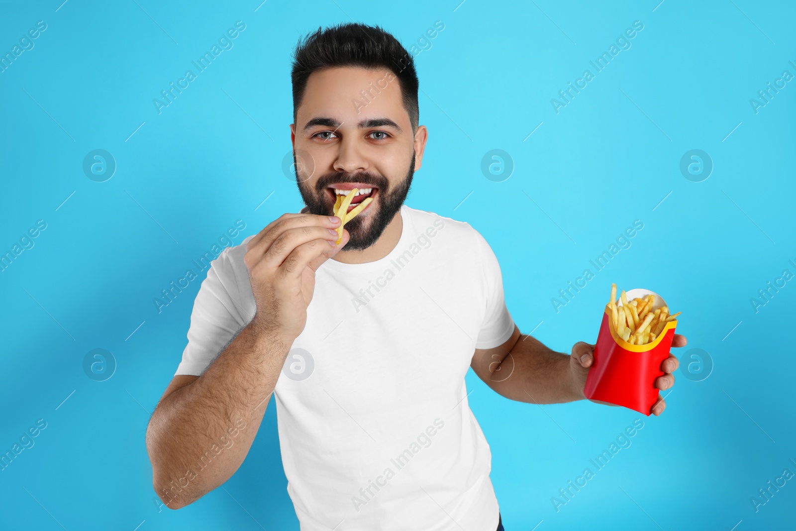 Photo of Young man eating French fries on light blue background