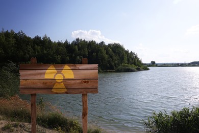 Image of Radioactive pollution. Yellow warning sign with hazard symbol near river outdoors