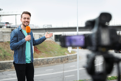 Photo of Young male journalist with microphone working on city street