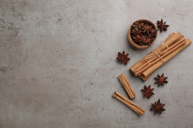 Aromatic cinnamon sticks and anise on grey table, flat lay. Space for text