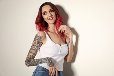 Beautiful woman with tattoos on arms against light background