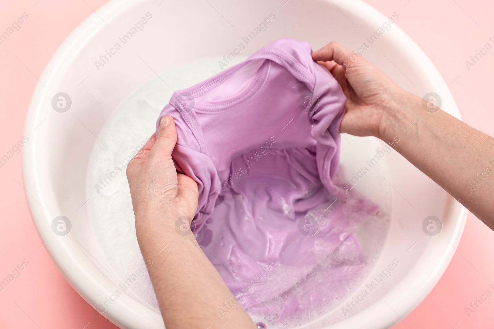 Photo of Woman washing baby clothes in basin on pink background, closeup