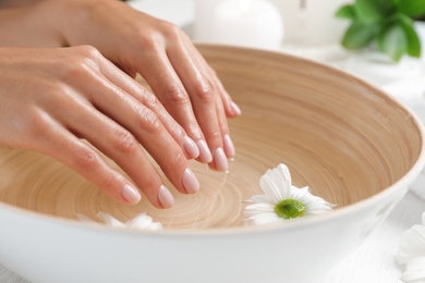 Photo of Woman soaking her hands in bowl of water and flowers, closeup with space for text. Spa treatment