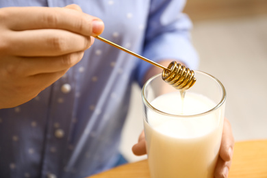 Woman adding honey to milk at table, closeup