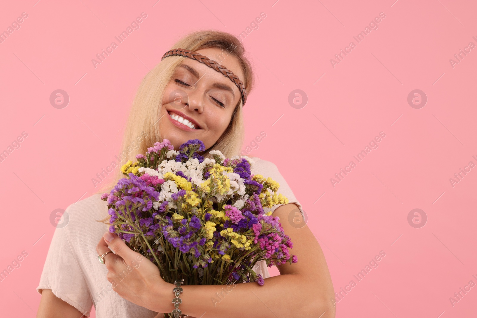 Photo of Portrait of smiling hippie woman with bouquet of flowers on pink background. Space for text