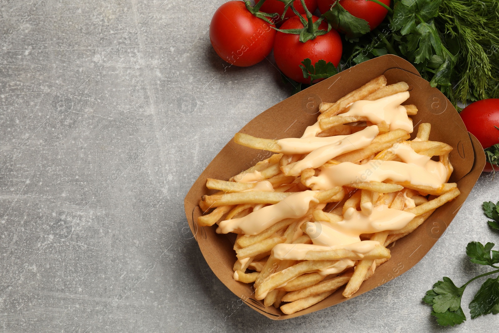 Photo of Tasty potato fries, cheese sauce in paper container and products on grey table, top view. Space for text