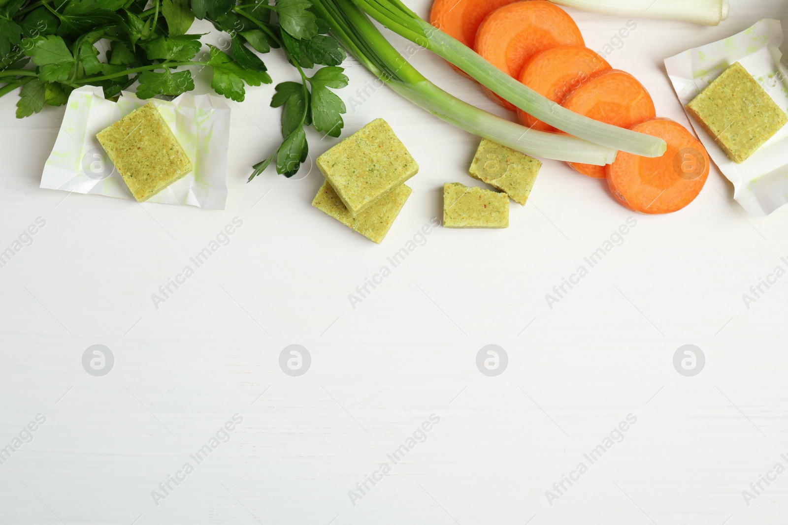 Photo of Bouillon cubes and other ingredients on white wooden table, flat lay. space for text