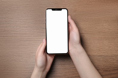 Photo of Woman holding smartphone with blank screen at wooden table, top view. Mockup for design