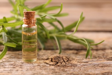 Photo of Aromatic essential oil in bottle and rosemary on wooden table, closeup. Space for text