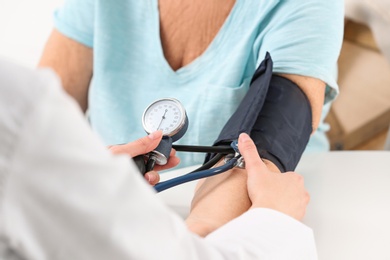 Nurse measuring blood pressure of elderly woman at table, closeup. Assisting senior generation