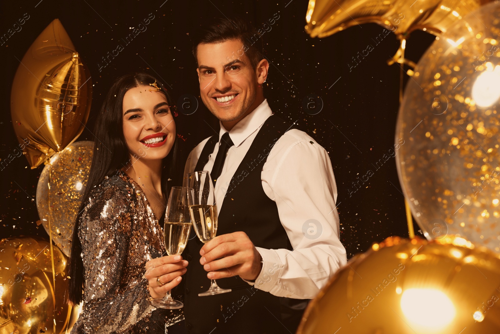 Photo of Happy couple with glasses of sparkling wine celebrating New Year on black background