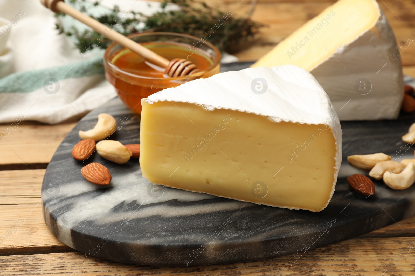 Photo of Tasty Camembert cheese with honey and nuts on wooden table, closeup