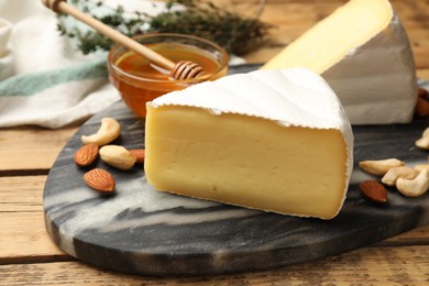 Photo of Tasty Camembert cheese with honey and nuts on wooden table, closeup