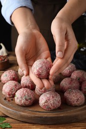 Photo of Woman making fresh raw meatballs at wooden table, closeup