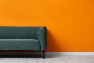 Stylish sofa near orange wall, space for text. Interior design