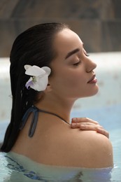 Beautiful woman with orchid flower in spa swimming pool