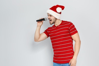 Photo of Young man in Santa hat singing into microphone on color background. Christmas music