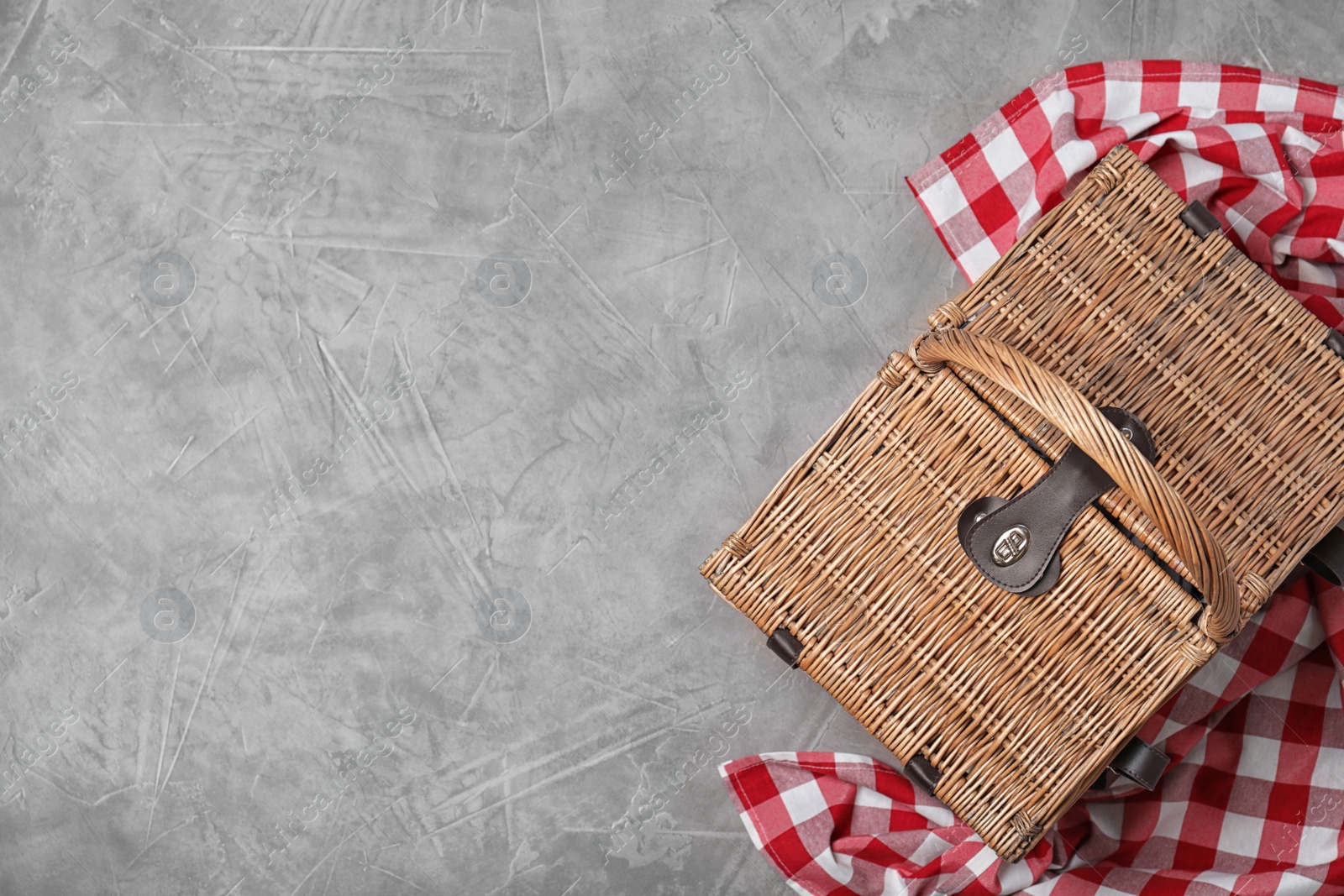 Photo of Checkered tablecloth and closed wicker picnic basket  on stone surface, top view. Space for text