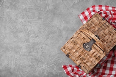 Photo of Checkered tablecloth and closed wicker picnic basket  on stone surface, top view. Space for text