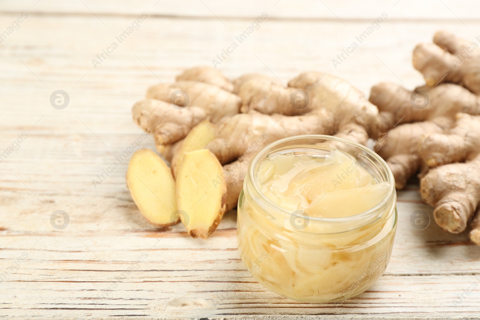 Photo of Spicy pickled ginger and root on white wooden table, space for text