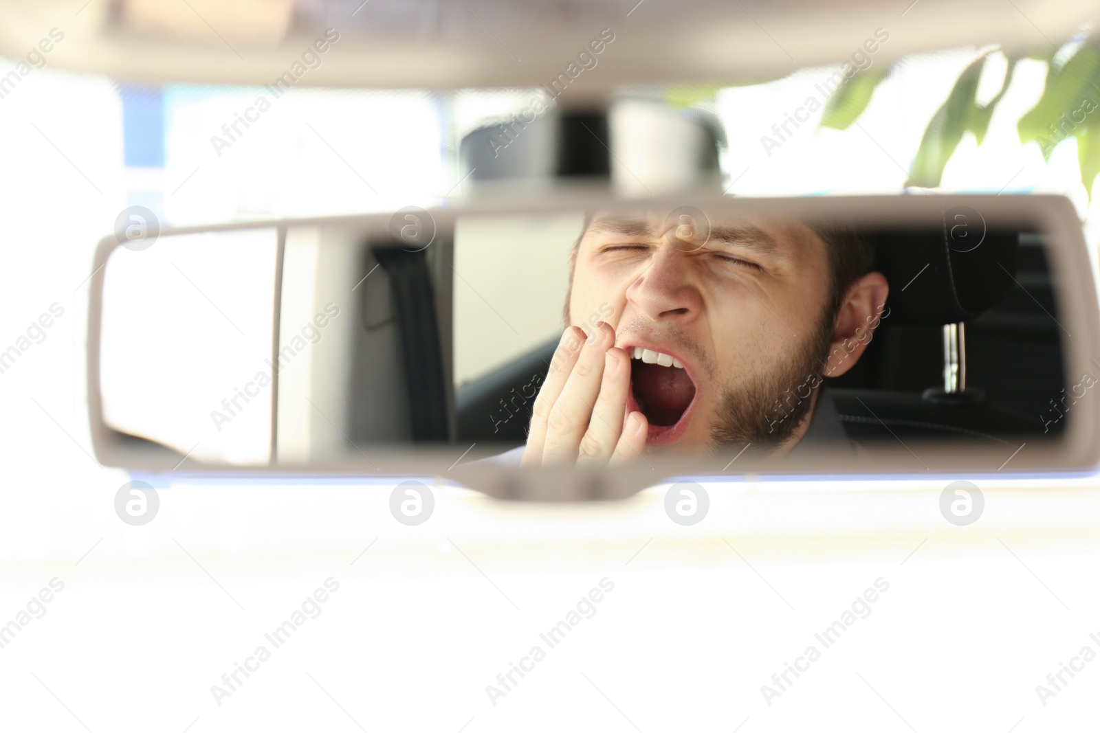 Photo of Tired man yawning while driving, reflection in rearview mirror