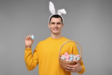 Easter celebration. Handsome young man with bunny ears and painted eggs on grey background
