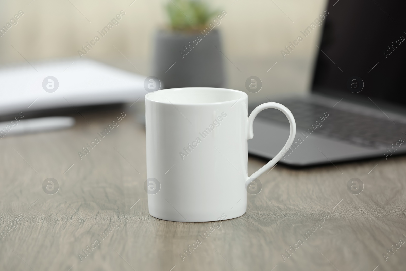 Photo of White ceramic mug and laptop on wooden table indoors