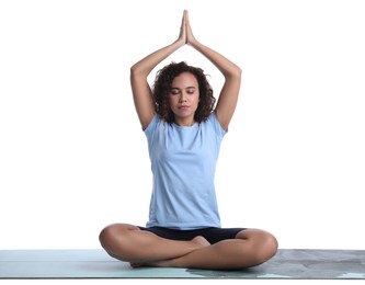 Beautiful African-American woman meditating on yoga mat against white background